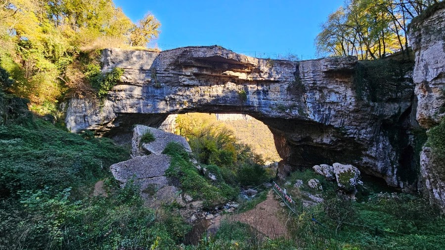 The Ponte di Veja, the great natural rock arch of the Lessinia, with blue sky and autumn woodland
