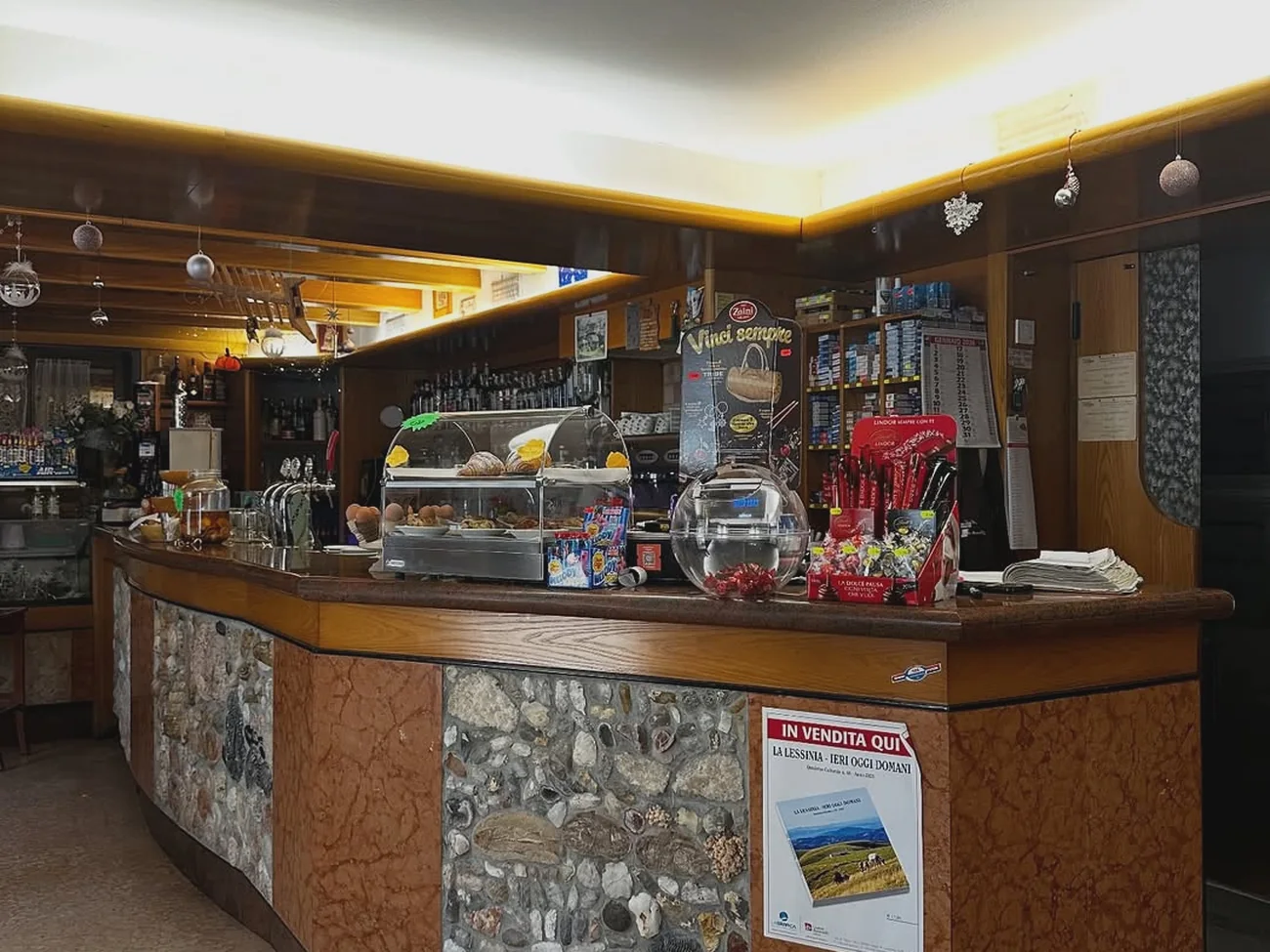 Il bancone del bar della trattoria con la vetrinetta e il fronte in pietra con i fossili