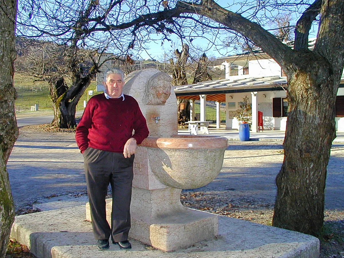 The double-basin stone fountain, with a carved horse's head and a face
